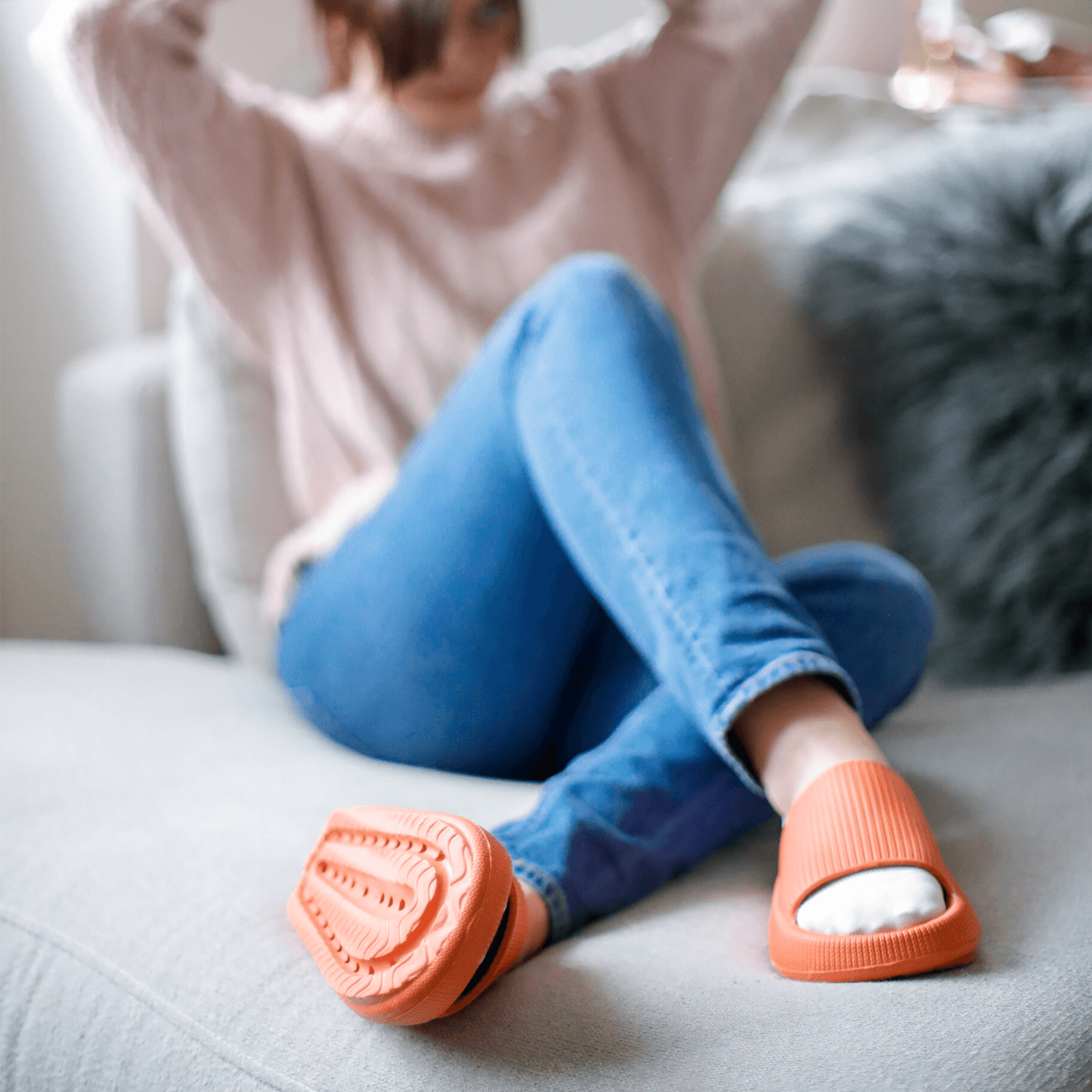 Dame sitter i sofa med oransje Soft Slippers på føttene